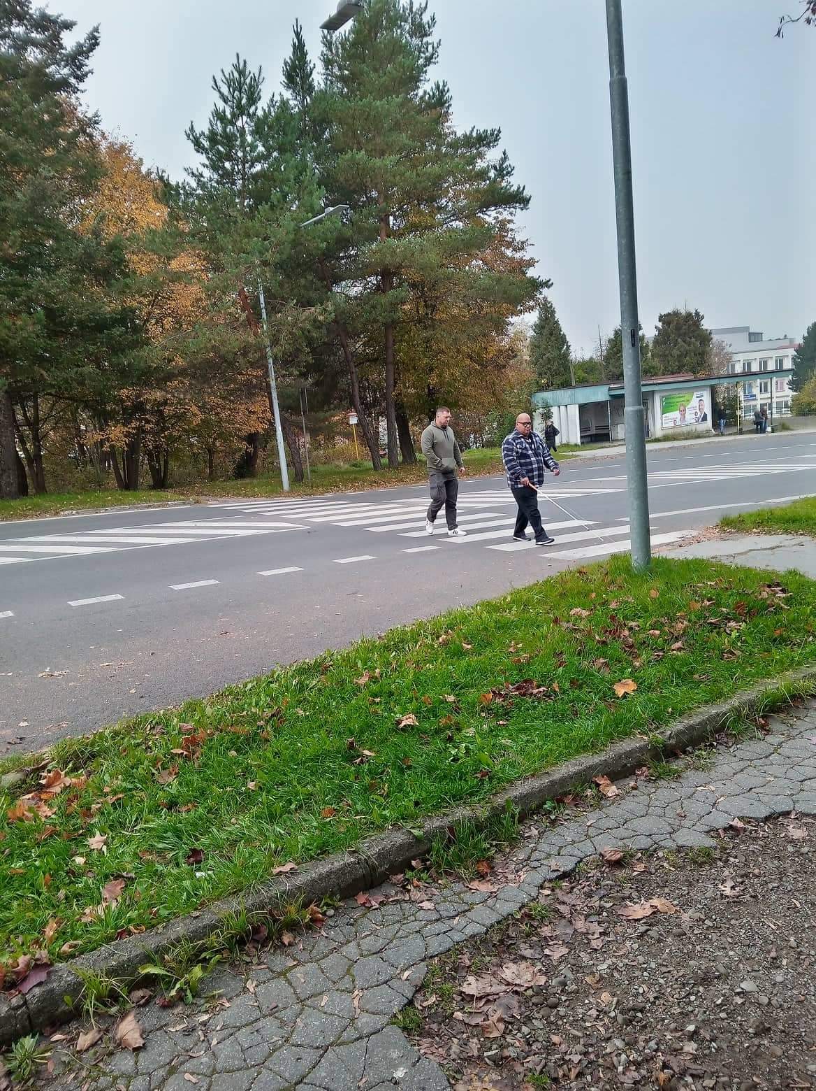 Muž s bielou palicou prechádza cez cestu.